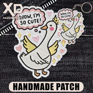 May include: Embroidered patch featuring a cartoon goose with a crown, yellow wings, and the text "WOW, I'M SO CUTE!". Includes a smaller keychain version. The patch is white with pink, yellow, and black accents. The words "HANDMADE PATCH" are at the bottom.