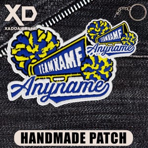 May include: Embroidered patch with a blue and yellow megaphone design, featuring the text "TEAM XAMF" and "Anyname". The patch also includes two pom-poms and the words "HANDMADE PATCH".