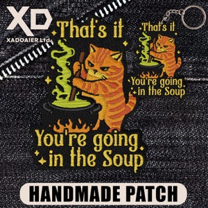 May include: Embroidered patch showing an orange tabby cat stirring a cauldron of green liquid, with the text "That's it" and "You're going in the Soup." A smaller keychain version is also visible. The patch is labeled "HANDMADE PATCH."