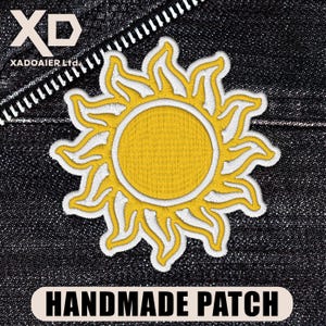 May include: A yellow sun-shaped embroidered patch with a white border, displayed on a dark denim fabric. The patch has the text "HANDMADE PATCH" in white on a black banner. The logo "XD XADOAIER Ltd." is in the upper left corner.