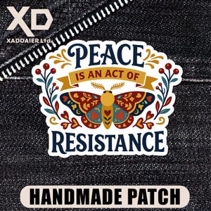 May include: A handmade patch with the text "PEACE IS AN ACT OF RESISTANCE" and a colorful butterfly design. The patch has a white border and is set against a dark denim background.