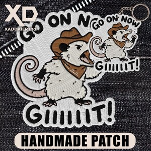 May include: Embroidered patch featuring a cartoon opossum wearing a cowboy hat and bandana, with the text "GO ON GIT!" and "HANDMADE PATCH". The design includes a smaller keychain version of the opossum.