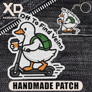 May include: Embroidered patch and keychain featuring a white duck riding a scooter, holding a coffee cup, and wearing a green backpack. The text "Off To Find Veins" is above the duck. The patch has the text "HANDMADE PATCH" at the bottom.
