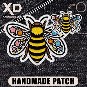 May include: Embroidered bee patch with yellow and black stripes, floral wing accents, and the text "HANDMADE PATCH." A smaller bee keychain with similar design is also shown. The patch is on a dark denim background.