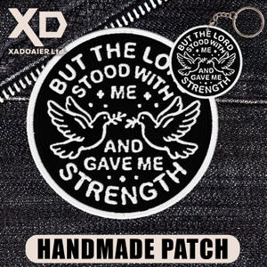 May include: A black and white patch and keychain set. The patch features two doves with olive branches and the text "BUT THE LORD STOOD WITH ME AND GAVE ME STRENGTH". The keychain has the same design. The bottom of the image reads "HANDMADE PATCH".