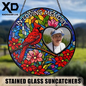 May include: A round stained glass suncatcher with a red cardinal perched on a branch, surrounded by colorful flowers and stained glass. The text "IN LOVING MEMORY" arches across the top. A heart-shaped photo frame is in the center. The text "STAINED GLASS SUNCATCHERS" is at the bottom.