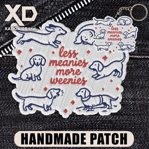 May include: Embroidered patch featuring dachshund dog illustrations in blue and white, with the text "less meanies more weenies" in red. The patch is handmade and includes a keychain attachment.