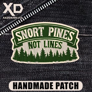 May include: Embroidered patch with the text "SNORT PINES NOT LINES" in white on a green banner, with a green forest design at the bottom. The patch also has the words "HANDMADE PATCH" in a white rectangle. The background is a dark denim fabric.
