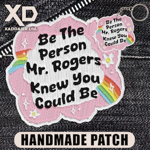 May include: A handmade patch with the text "Be The Person Mr. Rogers Knew You Could Be" in black on a pink cloud-shaped design. A smaller keychain with the same text and a rainbow is attached.