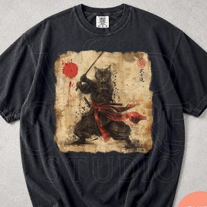 May include: A black short-sleeve t-shirt featuring a graphic print of a cat dressed as a samurai holding a sword. The design includes a red circular sun, a red sash, and Japanese characters. The shirt has a crew neckline and a faded, vintage-style finish.
