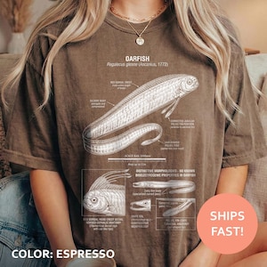 以下が含まれることがあります： エスプレッソ色のTシャツ。オアフィッシュの詳細な科学イラストが描かれており、解剖図やテキストが含まれています。「OARFISH」と「Regalecus glesne」の文字も含まれています。Tシャツの色は「COLOR: ESPRESSO」と表示されています。
