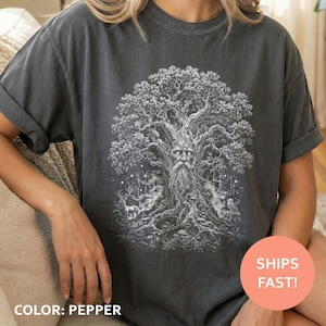 May include: A charcoal gray short-sleeve t-shirt featuring a detailed white graphic print of an ancient tree with a human face integrated into its trunk, surrounded by forest elements including a deer and an owl in a woodland setting.