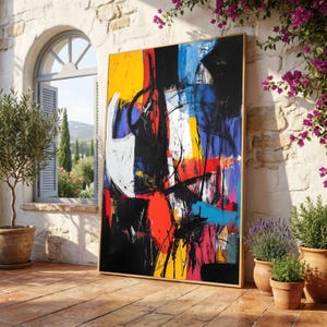 May include: Large abstract painting with a gold frame. The artwork features bold brushstrokes in yellow, black, red, white, blue, and turquoise. The painting is leaning against a stone wall on a brick patio, with potted plants nearby.