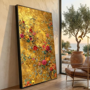 Könnte beinhalten: Ein großes gerahmtes Kunstwerk mit einem goldenen, strukturierten Hintergrund und farbenfrohen Blumenranken. Die Blumen sind in Rot, Rosa, Gelb und Blau gehalten. Das Kunstwerk lehnt an einer Wand in der Nähe eines Fensters mit Meerblick.