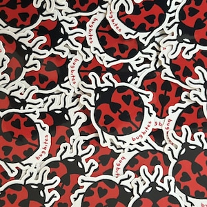 May include: A collection of stickers featuring a ladybug design. The ladybugs have red bodies with black heart-shaped spots and black heads. The stickers have a white border with the text "bug bites".