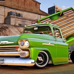 May include: A vintage green pickup truck with a raised bed, showcasing a wooden interior. The truck has chrome accents, a white bumper, and custom wheels. The background includes a warehouse and a cloudy sky.