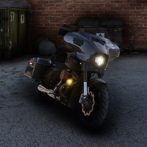 Puede incluir: Una motocicleta negra con carenado, alforjas y un neumático delantero grande. La motocicleta tiene un faro y intermitentes. Está estacionada sobre una superficie gris frente a una pared de ladrillos.