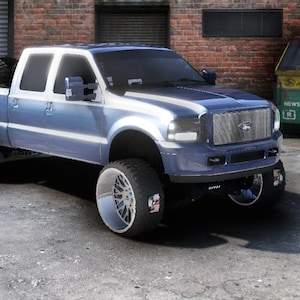 Puede incluir: Una camioneta azul con ruedas y neumáticos cromados grandes y personalizados. La camioneta tiene un techo blanco y un neumático de repuesto en la caja. El vehículo está estacionado sobre una superficie de hormigón.