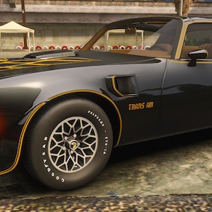 Könnte beinhalten: Ein schwarzes Trans Am-Auto mit goldenen Akzenten. Das Auto hat ein schlankes Design mit dem Schriftzug "TRANS AM" an der Seite. Die Räder haben ein einzigartiges Sternmuster. Das Auto steht auf einer Betonoberfläche.