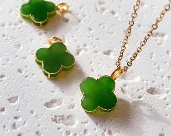 May include: A gold chain necklace featuring a four-leaf clover pendant with a smooth green stone inlay, accompanied by two matching clover charms. Each piece is framed in a thin gold border, creating a cohesive set of jewellery with a clover motif.