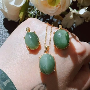 May include: A jewelry set featuring a necklace and matching earrings. The set includes a gold chain necklace with a pendant and two oval-shaped earrings. Each piece has a gold setting and a large, oval, green gemstone.