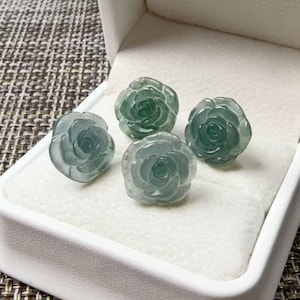 Peut inclure: Quatre ornements en pierre verte sculptée en forme de rose disposés dans une boîte à bijoux blanche. Chaque pièce présente des détails de pétales superposés complexes avec une finition lisse et polie et des qualités translucides.