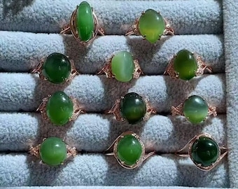 May include: A collection of ten rings featuring smooth, oval-shaped green gemstones set in rose-colored metal bands. Each ring displays a unique shade of green, ranging from light lime to deep forest tones, arranged in a grid pattern.