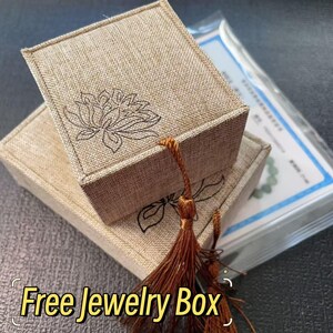 May include: Two beige linen jewelry boxes stacked, one atop the other. Each box features a floral design and a decorative tassel. The text "Free Jewelry Box" is displayed in a yellow font at the bottom of the image.