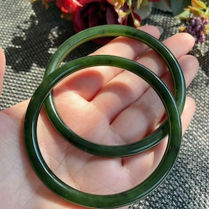 May include: Two smooth, circular bangles crafted from dark forest green stone. Each bangle features a polished, glossy finish with subtle variations in the deep green colour, showcasing a simple, continuous band design without any additional ornamentation.