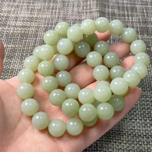May include: A stretch bracelet composed of numerous smooth, round, pale green beads. The beads have a polished, semi-translucent finish and are strung together in a circular formation, creating a continuous loop of light green stone spheres.