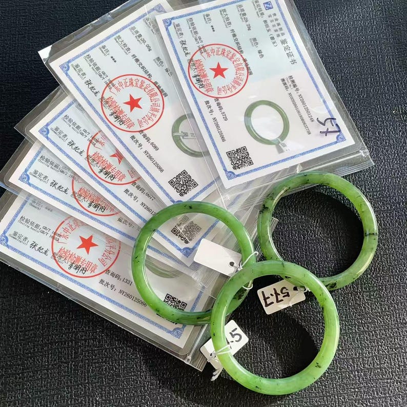 May include: Three green jade bangles with visible inclusions are displayed alongside several official certificates. The certificates feature red seals and Chinese text. The bangles are a vibrant green color and appear to be polished.