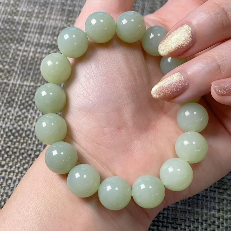 May include: A bracelet composed of smooth, round, pale green beads with a polished finish. The beads are uniform in size and strung together in a circular shape, displaying a soft, translucent quality and a consistent light green color throughout.