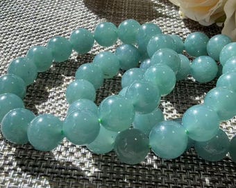 May include: A stretch bracelet composed of smooth, round, light green beads with a subtle translucent quality. The beads are strung together in a circular loop, showcasing a consistent pale mint color and a polished, reflective surface finish.