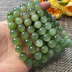 May include: A strand of smooth, round, translucent light green beads. The beads exhibit a soft, polished luster and varying shades of pale to medium green, creating a uniform appearance throughout the circular, spherical gemstone arrangement.