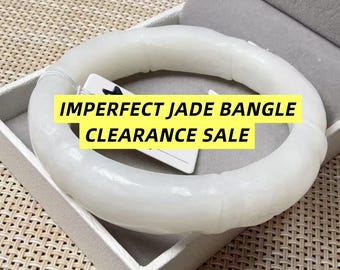 May include: A white jade bangle with a smooth, segmented bamboo-like texture. A white tag is attached to the bangle with the black text IMPERFECT JADE BANGLE CLEARANCE SALE printed on a yellow background overlaying the center of the jewelry piece.