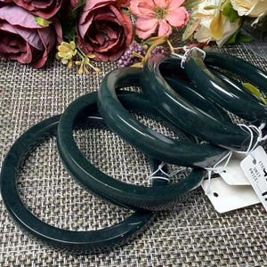 Op de afbeelding: Een set van vier donkergroene, gladde, ronde armbanden die in een rij zijn gestapeld. Elke armband heeft een gepolijste afwerking en is bevestigd aan een klein wit papieren label met de gedrukte tekst ITEM en UNIT PRICE zichtbaar.