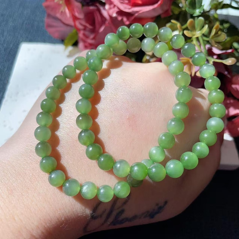 May include: Two jade green beaded bracelets. Each bracelet is made of round, polished beads. The bracelets are a light green colour and appear to be made of a smooth, translucent material. The bracelets are displayed on a light-coloured surface.