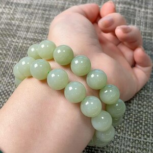 May include: A double-strand bracelet composed of smooth, polished, pale green jade-like beads. The spherical beads are uniform in size and feature a glossy, reflective surface that catches the light, creating a soft, translucent appearance throughout.