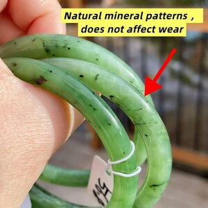 May include: Three jade green bangles with natural mineral patterns and black inclusions are displayed. The text in the image reads: "Natural mineral patterns, does not affect wear."