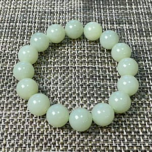 May include: A circular bracelet composed of smooth, polished, pale mint green spherical beads. The beads are uniform in size and arranged in a continuous loop, reflecting light on their glossy surfaces, creating a consistent and rounded appearance.