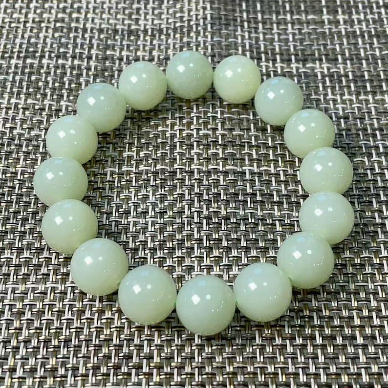 May include: A circular bracelet composed of smooth, polished, pale mint green spherical beads. The beads are uniform in size and arranged in a continuous loop, reflecting light on their glossy surfaces, creating a consistent and rounded appearance.