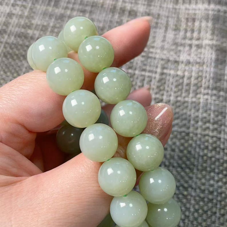 May include: A bracelet composed of smooth, round, pale green beads with a polished finish. The beads are strung together in a circular arrangement, displaying a consistent light mint-green hue and a reflective surface that catches the light.