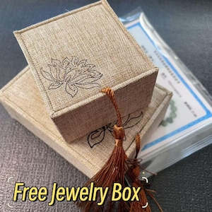 May include: Two beige linen jewelry boxes stacked, each with a lotus flower design. A brown tassel hangs from the top box. The text "Free Jewelry Box" is at the bottom of the image.