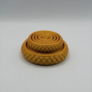 May include: A stack of three golden-yellow, circular objects. The largest has a textured, rounded edge. The middle one is smaller, with a similar design. The smallest is a series of concentric circles. The objects are likely decorative or functional.