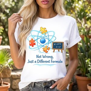 May include: White t-shirt featuring a science-themed graphic with a blue atom design, puzzle pieces, and a small chalkboard with equations. The shirt also has the text "Not Wrong, Just a Different Formula".