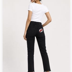May include: A white short-sleeved t-shirt paired with black denim jeans featuring a frayed hem and a comic-style patch on the back pocket that reads DOPE in red letters inside a white cloud shape, worn with plain white sneakers.