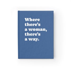 Op de afbeelding: Een blauw notitieboek met harde kaft en de witte tekst "Where there's a woman, there's a way." op de voorkant. Het notitieboek heeft een effen blauwe rug en een rechthoekige vorm met een egale afwerking over het gehele oppervlak.