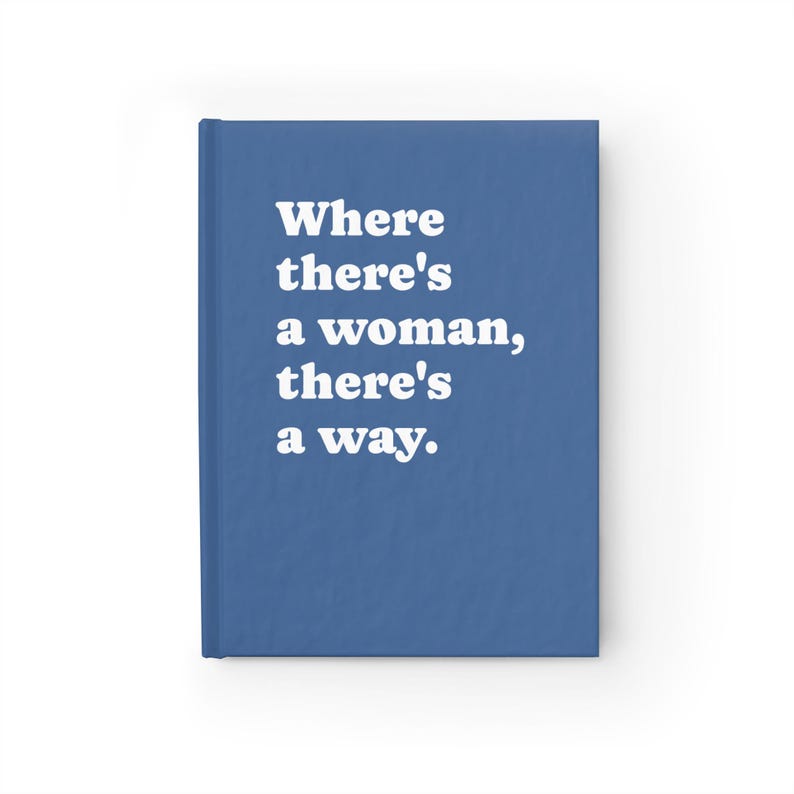 Op de afbeelding: Een blauw notitieboek met harde kaft en de witte tekst "Where there's a woman, there's a way." op de voorkant. Het notitieboek heeft een effen blauwe rug en een rechthoekige vorm met een egale afwerking over het gehele oppervlak.