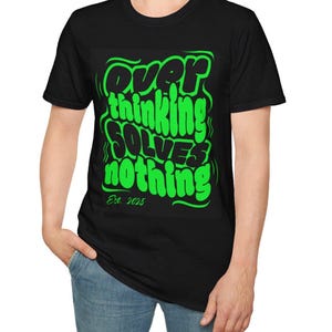Puede incluir: Camiseta negra con un gráfico verde neón que dice "Overthinking Solves Nothing" en una fuente audaz y estilizada. El texto "Est. 2025" está debajo. La camiseta la lleva una persona.