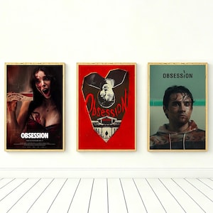 Puede incluir: Tres carteles de películas enmarcados con el título "Obsesión". Los carteles presentan imágenes de actores y diseños gráficos. Los carteles están en marcos dorados y se exhiben en una pared blanca.